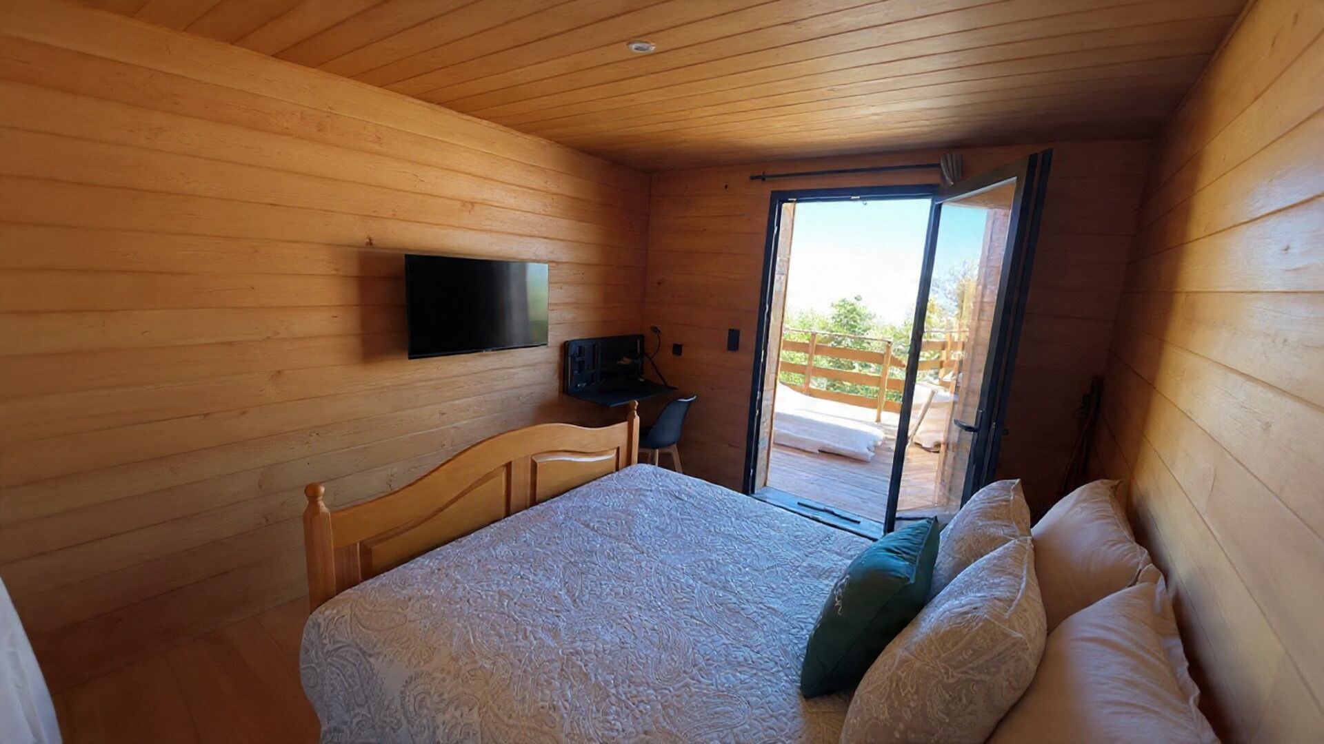 A wooden room with a bed, a desk, and a TV mounted on the wall.
