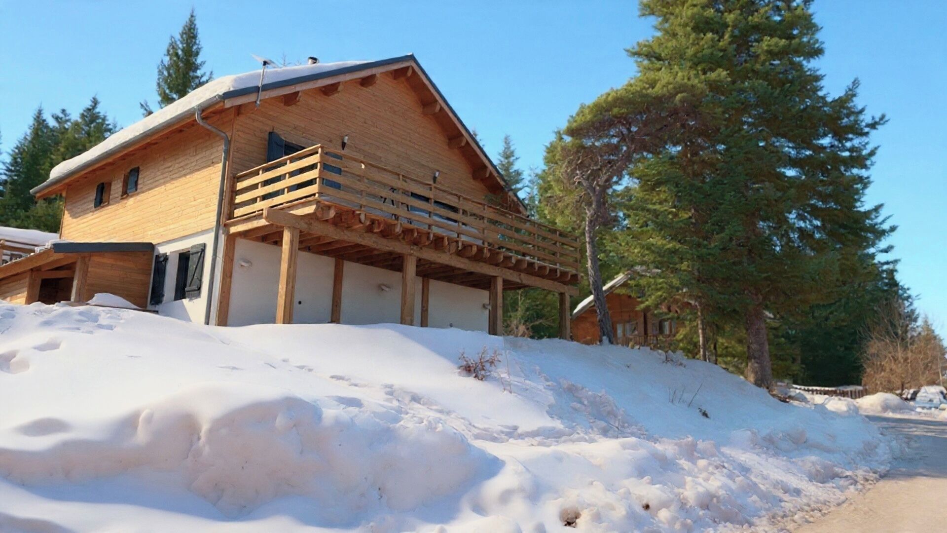 A wooden cabin with a balcony, surrounded by snow and trees.