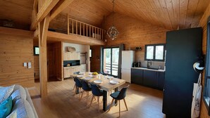 Una cabaña de madera con comedor, cocina y habitación en un altillo.