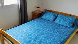 A bedroom with a bed, a nightstand, a window with curtains, and a wall-mounted light fixture. - Duplex apartment for seaside vacations (LE GRAU D'AGDE)