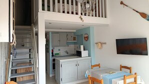 A spacious kitchen with white cabinets, a dining area with a table and chairs, and a loft bedroom with a balcony. - Duplex apartment for seaside vacations (LE GRAU D'AGDE)