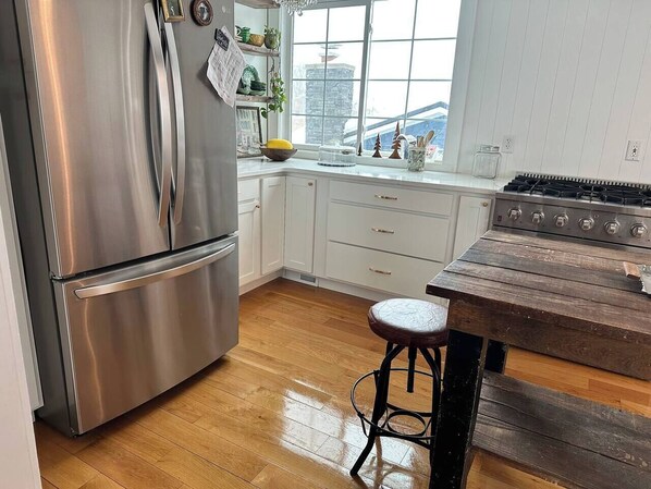 A kitchen with stainless steel appliances, white cabinetry, a wooden floor, and a rustic wooden table.