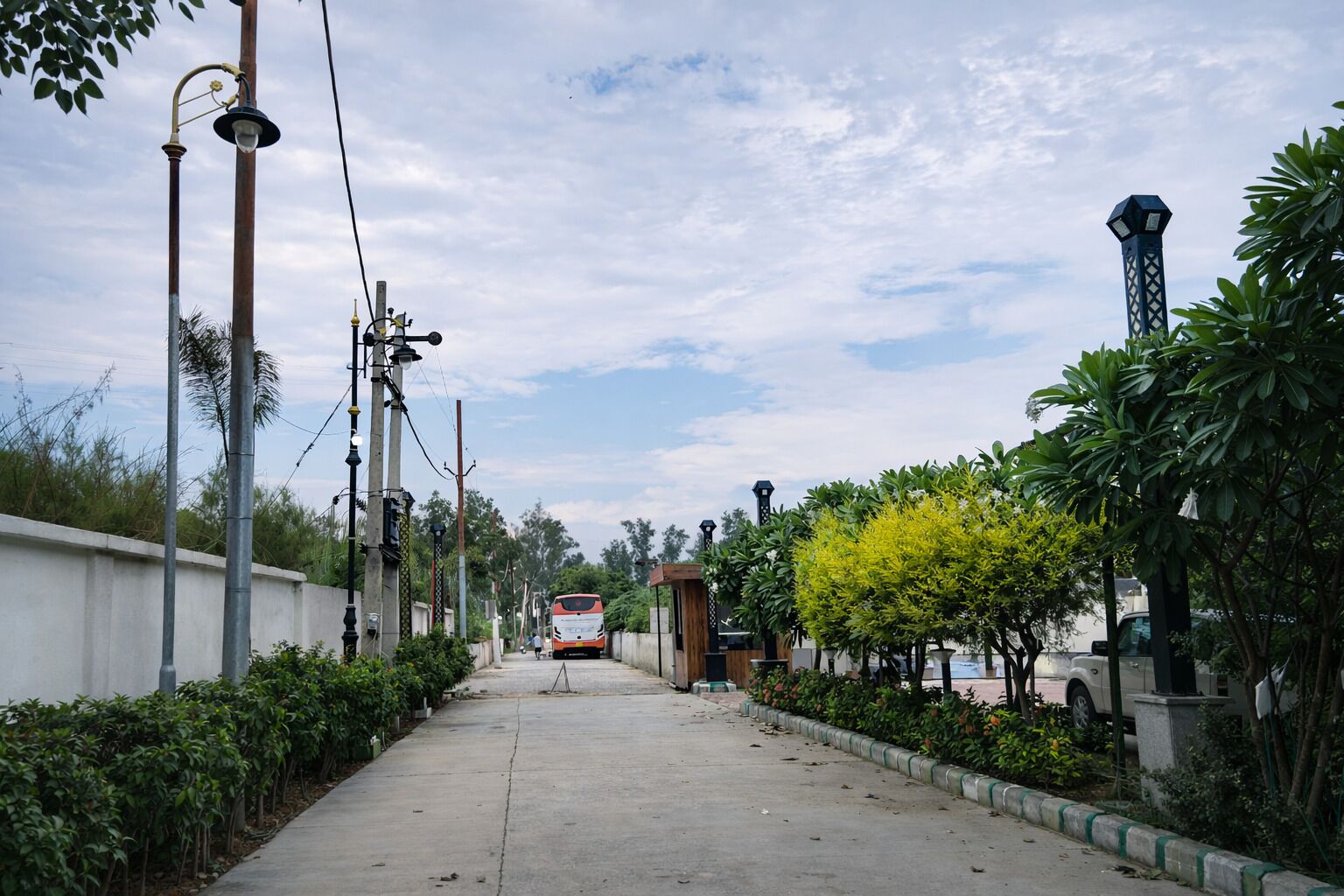 A pathway lined with street lamps and trees, leading to a bus stop.