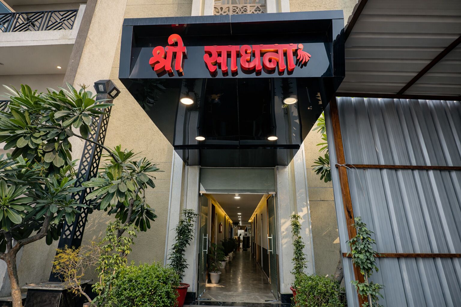 A hotel entrance with a sign in Hindi, a covered walkway, and potted plants.