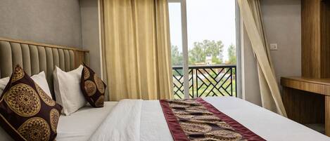 A hotel room with a large bed, a headboard, a window with curtains, an air conditioning unit, and a balcony with a railing.