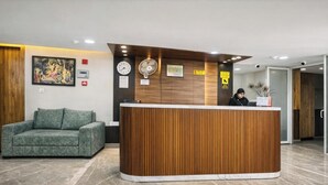 Un espace d’accueil avec un comptoir de réception en bois, un canapé vert, une horloge et un ventilateur fixé au mur.