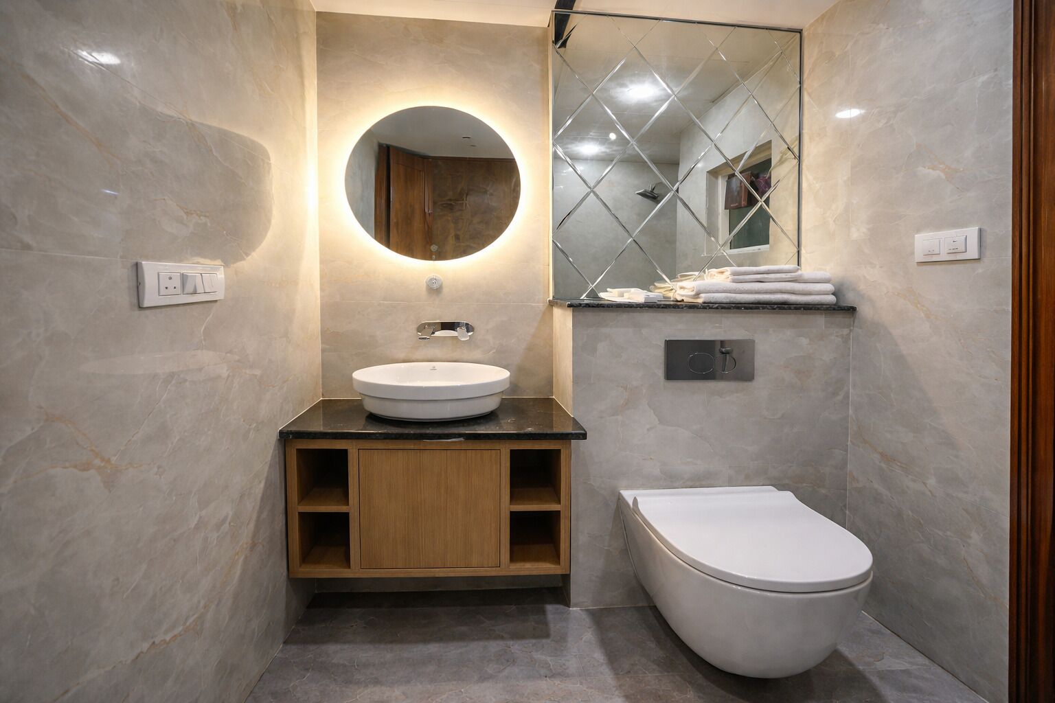 A modern bathroom with a round mirror, a sink, and a toilet.