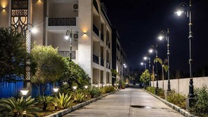 Vue nocturne d’un couloir d’hôtel à plusieurs étages, bien éclairé, avec un chemin en béton, des lampadaires décoratifs et un aménagement paysager luxuriant.