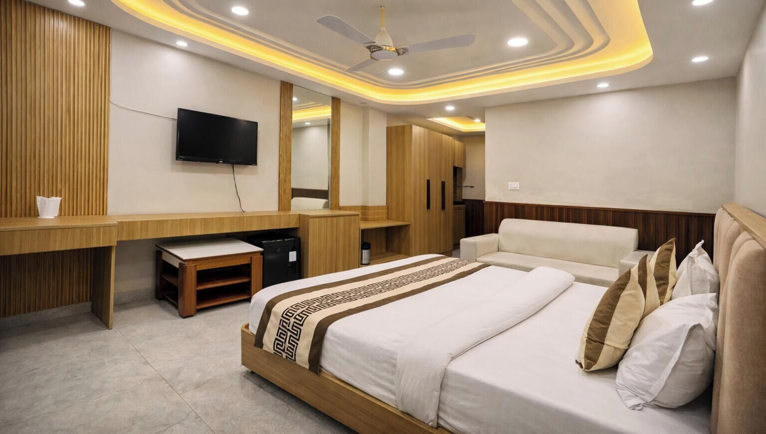 A hotel room with a bed, a desk, a television, and a ceiling fan.