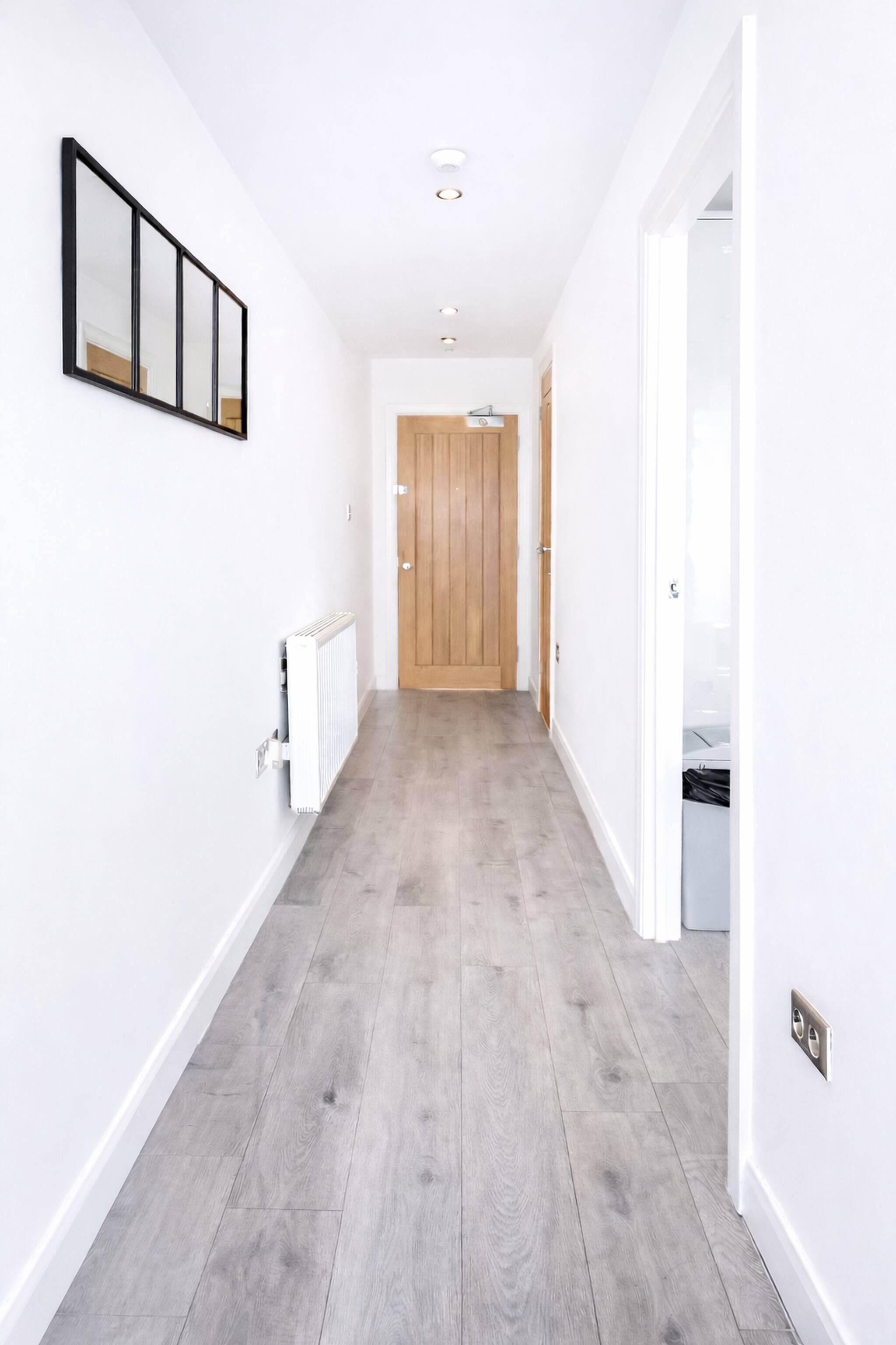 A hallway with a wooden floor, white walls, and a wooden door at the end.