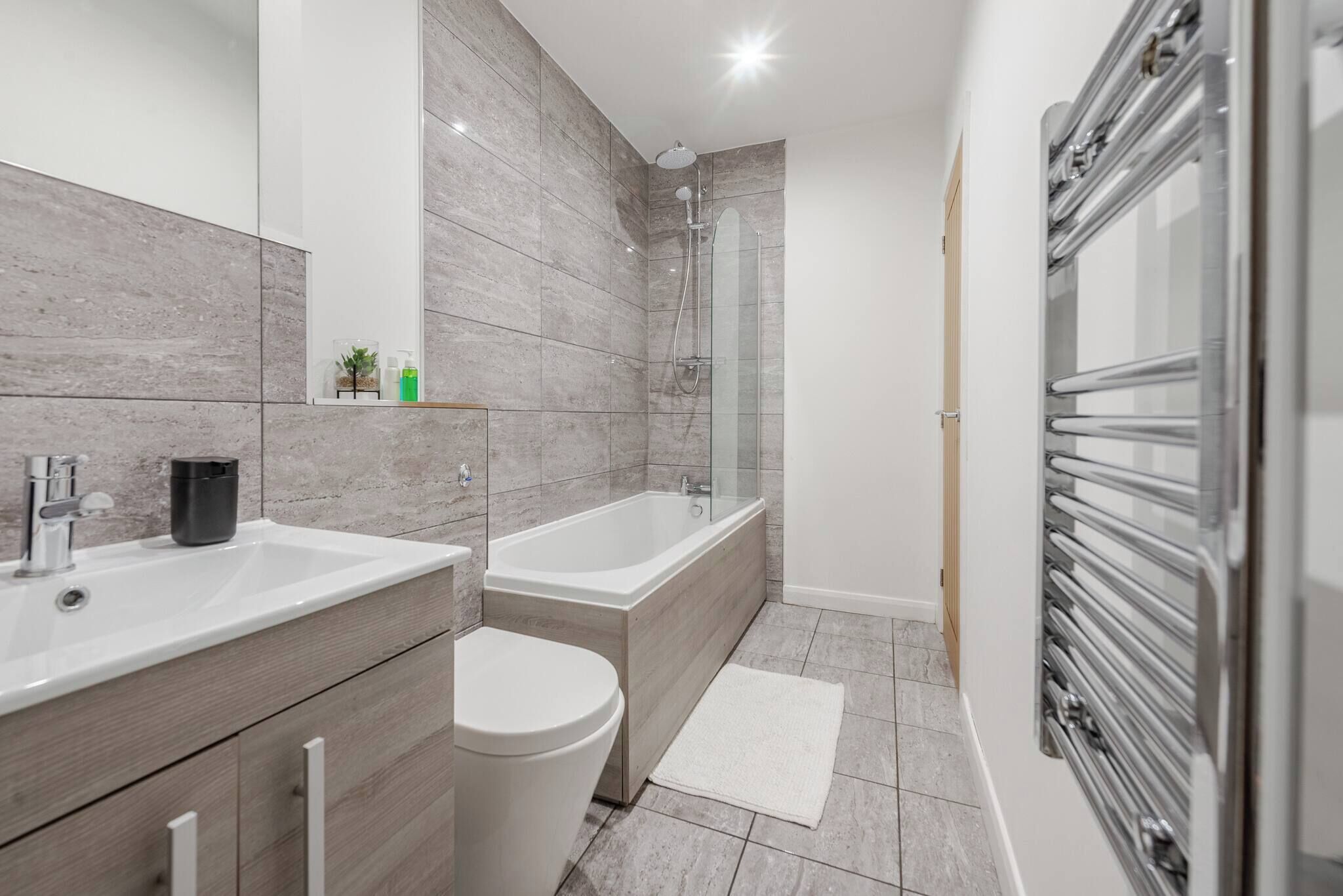 A modern bathroom with a large mirror, a bathtub, a toilet, and a shower.