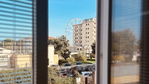 En vy genom ett fönster i en byggnad, med ett pariserhjul i bakgrunden, parkerade bilar och grönska.