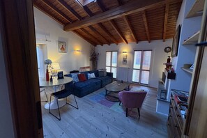 Un vaste espace de vie doté d’un plafond en bois, d’un canapé bleu, d’une table basse et d’un fauteuil rose.