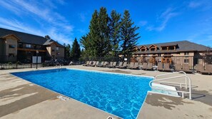 A swimming pool with lounge chairs, a lifeguard stand, and a building with a wooden facade. - Golf Course Studio Retreat (Radium Hot Springs)
