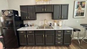 A kitchen with dark cabinets, a granite countertop, a sink with a gold faucet, and a microwave on the left. - Marilyn Monroe Vintage Suite (Logan)