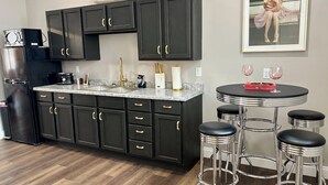 A modern kitchen with dark cabinets, a granite countertop, a black refrigerator, and a bar area with stools. - Marilyn Monroe Vintage Suite (Logan)