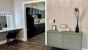 A modern kitchen with dark cabinets, a white countertop, and a vanity with a mirror and lights. - Marilyn Monroe Vintage Suite (Logan)