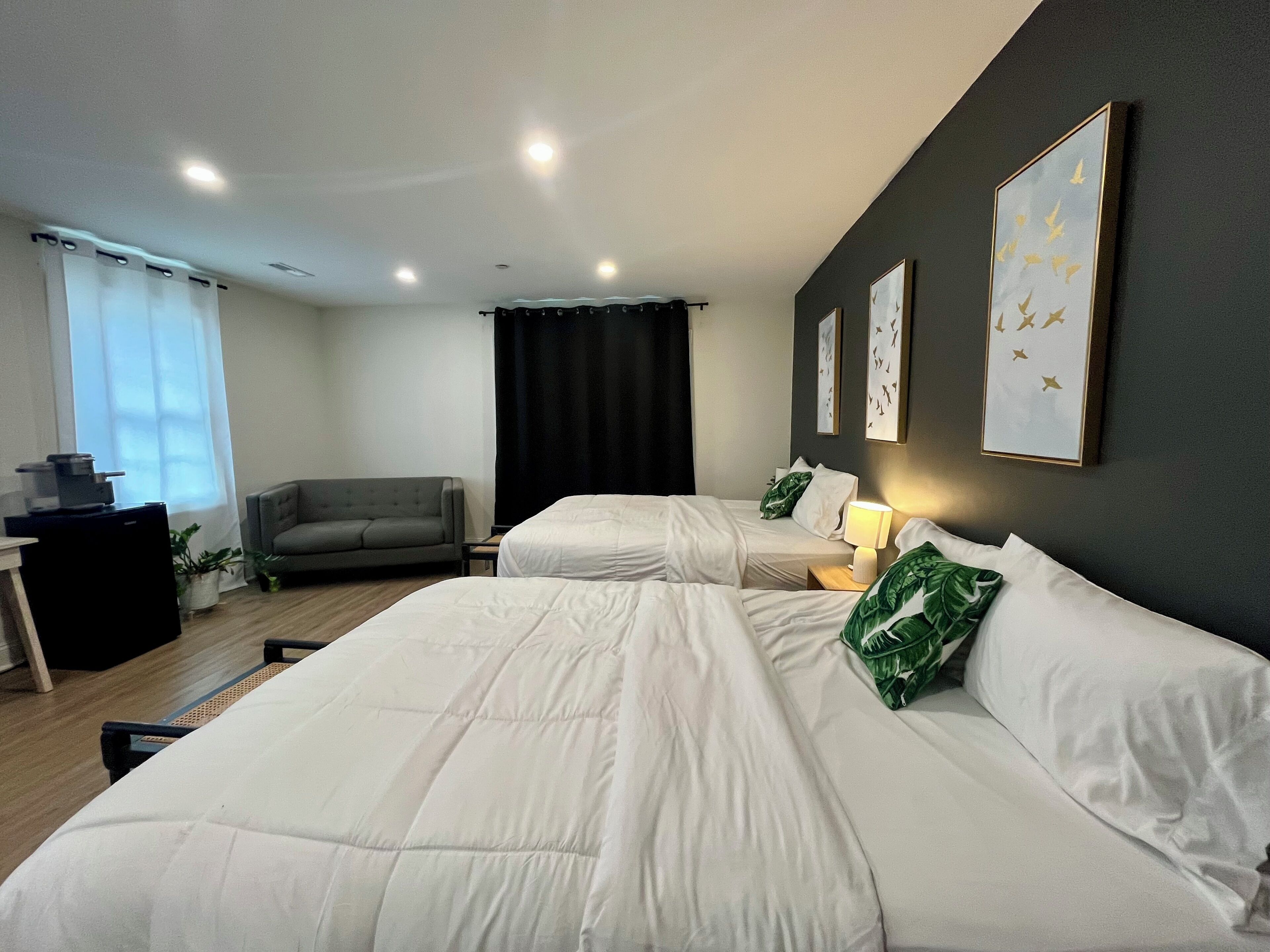 Hotellihuone, jossa on kaksi sänkyä, sohva, työpöytä ja ikkuna, jossa on verhot.
