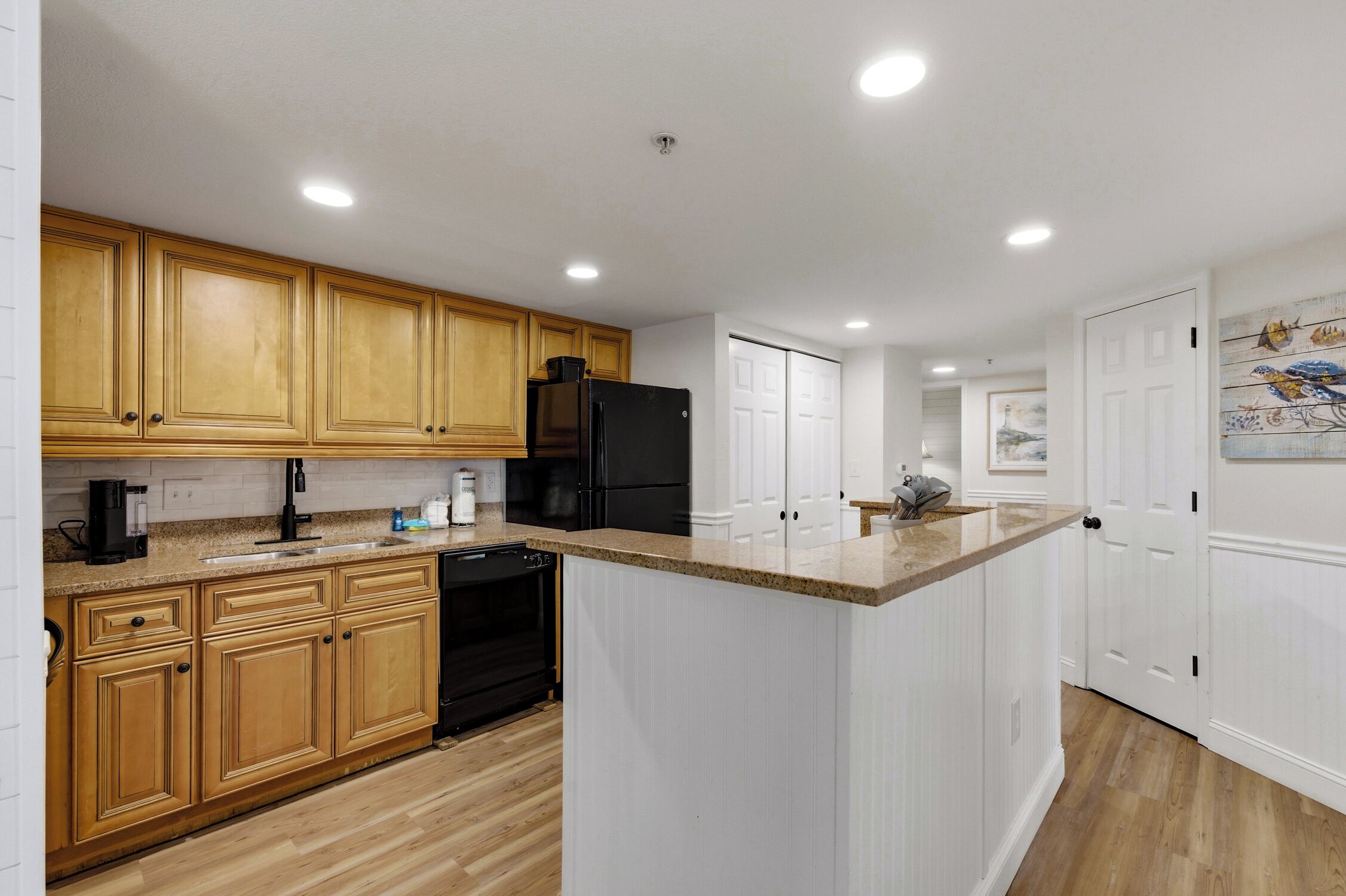 A kitchen with wooden cabinets, a black refrigerator, and a granite countertop.