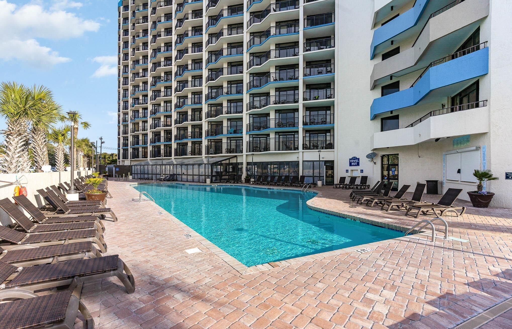 A hotel with a large outdoor swimming pool, multiple balconies, and lounge chairs.