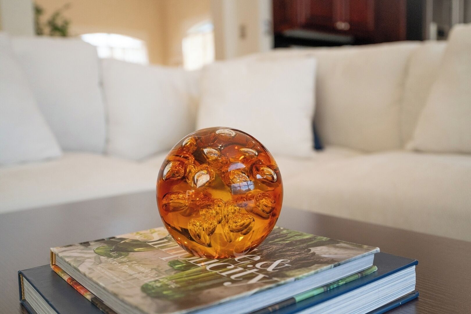 Uma esfera de vidro transparente com superfície refletora, colocada sobre uma pilha de livros em uma mesa.