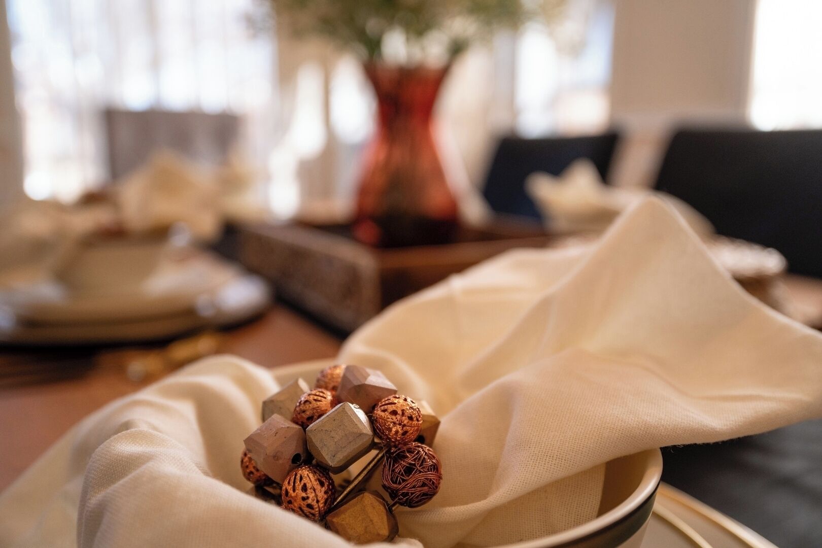 A table setting with a cloth napkin, a plate with decorative items, and a vase in the background.