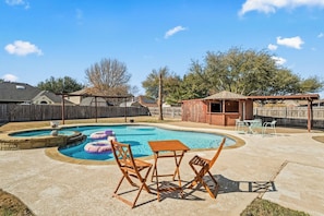 A backyard with a swimming pool, inflatable rings, a wooden table, and chairs. - Family 4BR Retreat | Pool • BBQ • Game Room (Grand Prairie)