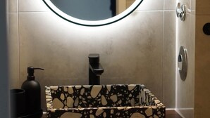 Ein Badezimmer mit einem rechteckigen Waschbecken, einem Spiegel mit Beleuchtung und einem Handtuchhalter im Hintergrund.