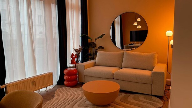 Ein modernes Wohnzimmer mit einer Couch, einem runden Couchtisch, einem Sessel und einem großen Spiegel an der Wand.