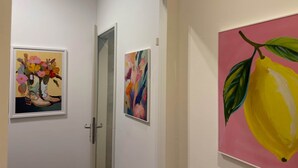 Ein Flur mit drei gerahmten Kunstwerken an den Wänden, einer Tür und einer rosafarbenen Wand rechts.
