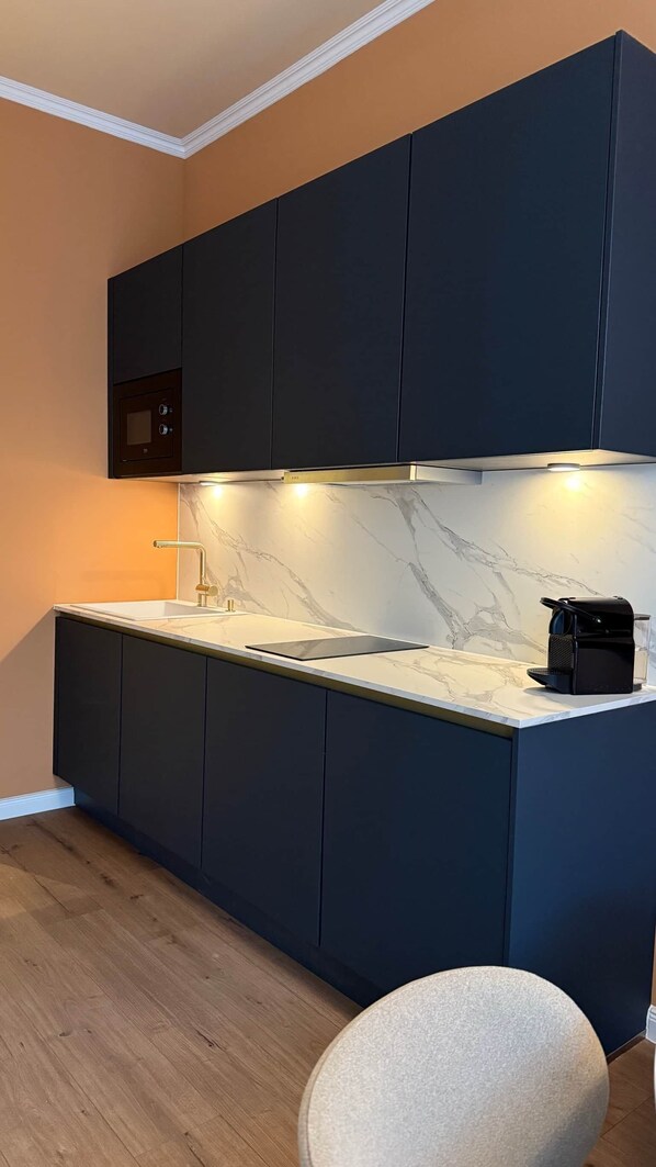 A modern kitchen with dark cabinetry, a marble countertop, and a built-in oven. - Atrium Apartments Aachen 3 (Aachen)