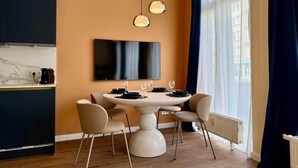 Ein moderner Essbereich mit einem runden Tisch, vier Stühlen, einer Kaffeemaschine und einem großen Flachbildfernseher an der Wand.