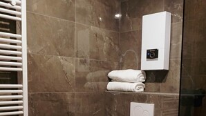 A modern bathroom with a marble wall, a toilet, a towel rack, and a glass shower enclosure. - Atrium Apartments Aachen 1 (Aachen)