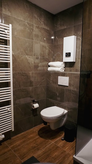 A modern bathroom with a marble wall, a toilet, a towel rack, and a glass shower enclosure. - Atrium Apartments Aachen 1 (Aachen)