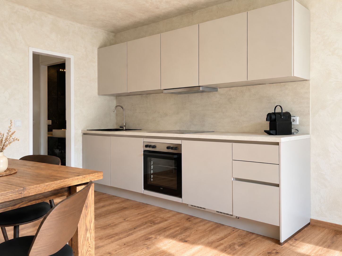 Una cocina compacta con armarios blancos, horno empotrado y cafetera sobre la encimera.