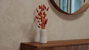 A wooden cabinet with a vase of dried plants on a textured wall. - Atrium Apartments Aachen 1 (Aachen)