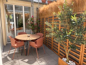 A patio with a round table and chairs, a wooden fence, and a potted plant. - Atrium Apartments Aachen 1 (Aachen)