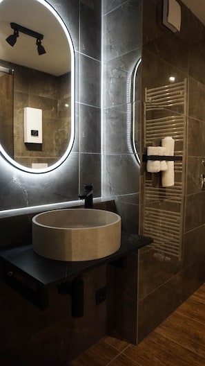 A modern bathroom with a round sink, a large mirror with integrated lighting, and a towel rack. - Atrium Apartments Aachen 1 (Aachen)