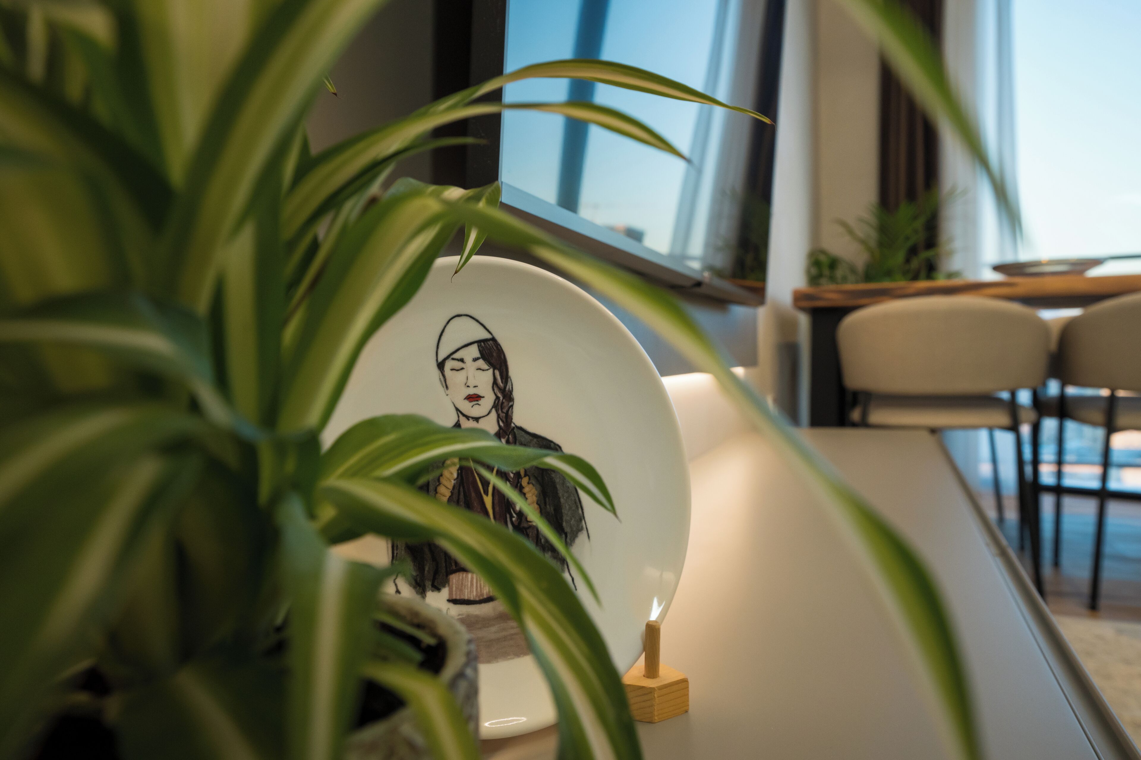 Een modern interieur met een witte tafel, een keramieken bord met een grafisch ontwerp en een potplant.