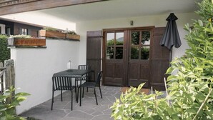 A patio with a table and chairs, a wooden door, and a hanging umbrella. - The small apartment (23 square meters) in a modern country house style (Reit im Winkl)