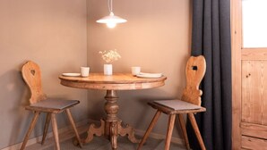 A round wooden table with two chairs, a hanging light fixture, and a vase with flowers. - The newly renovated apartment (30 m²) has a combined living and sleeping area (Reit im Winkl)