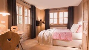 A bedroom with a bed, a desk, a chair, and a window with curtains. - The newly renovated apartment (30 m²) has a combined living and sleeping area (Reit im Winkl)