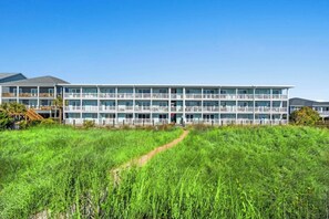 A multi-story hotel with a central entrance, surrounded by a grassy field and a clear sky. - Kings View Villas C2- Oceanfront 2BR- Cherry Grove (North Myrtle Beach)