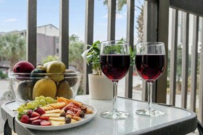 Ein Tisch mit einer Obstplatte und zwei Gläsern Rotwein, auf einem Balkon mit Blick auf Palmen und Gebäude.