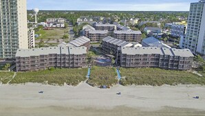 Een hotelcomplex aan de kust met meerdere gebouwen, een strand op de voorgrond en een heldere lucht.