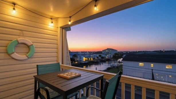 Varanda com mesa e cadeiras, vista para a orla com edifícios ao fundo durante o pôr do sol.
