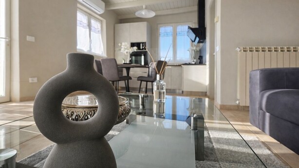 A modern living room with a glass coffee table, a dark-colored sofa, and a decorative vase. - "Calla Bianca "Borgo al Sole smart working, private pool nature and relaxation (Colombiera-Molicciara)