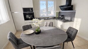 A modern kitchen with a dining area, featuring a round table, grey chairs, and a potted orchid. - "Calla Bianca "Borgo al Sole smart working, private pool nature and relaxation (Colombiera-Molicciara)