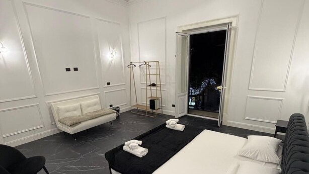 Una habitación de hotel moderna con una cama grande, un área de descanso con sofá y sillones, una mesita y un armario con espejo.