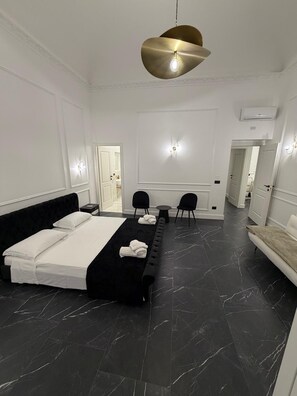 A modern hotel room with a large bed, a black leather sofa, a small round table, and a unique pendant light. - Four Rooms Luxury Suite (Palermo)
